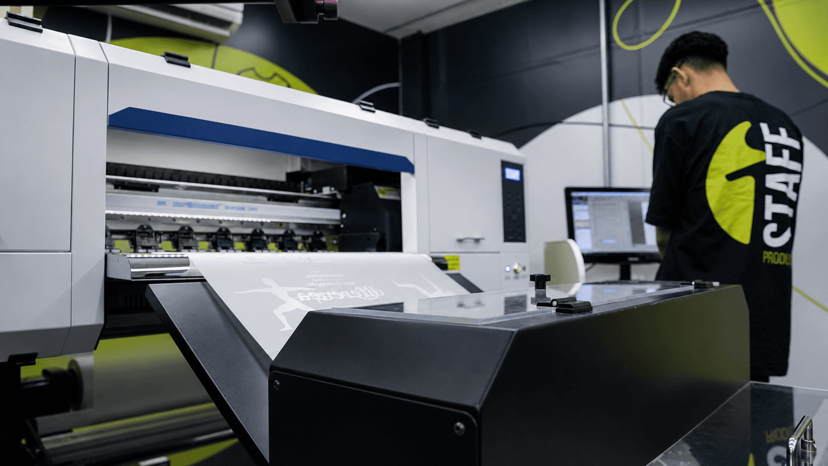 Großformat-UV-Drucker in Betrieb in der Fabrik von Innovation, ein Mitarbeiter prüft den Auftrag am Computer