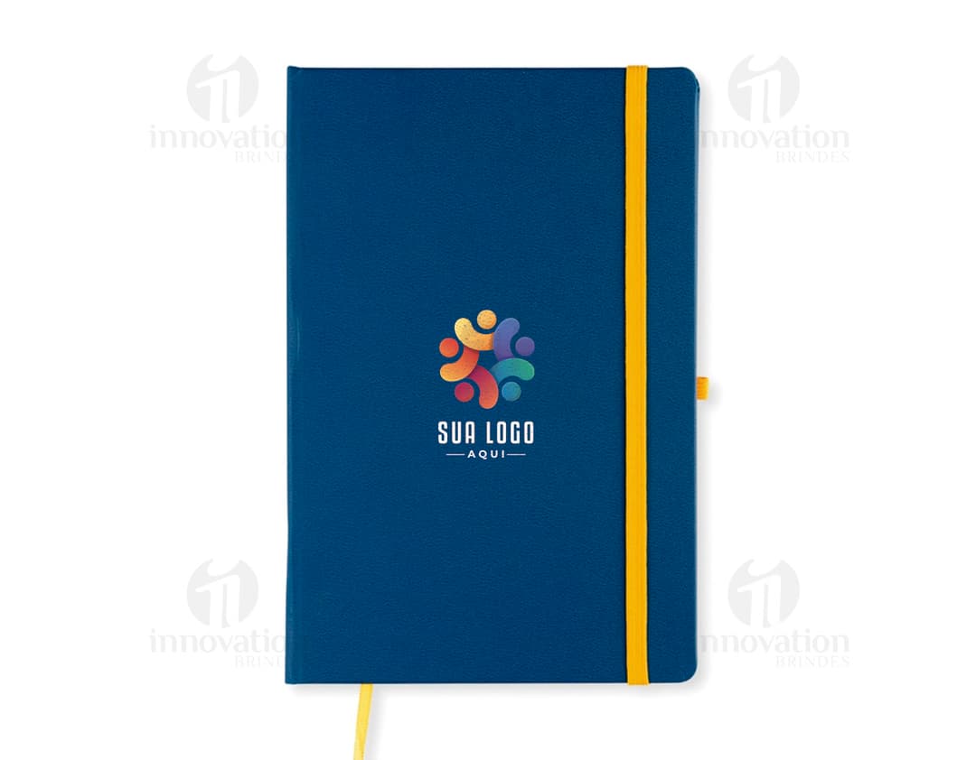 Notebook amarelo aberto com papel pautado em um escritório, ao lado de um modem, um telefone e um copo de bebida.