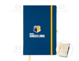 Notebook amarelo aberto com papel pautado em um escritório, ao lado de um modem, um telefone e um copo de bebida.