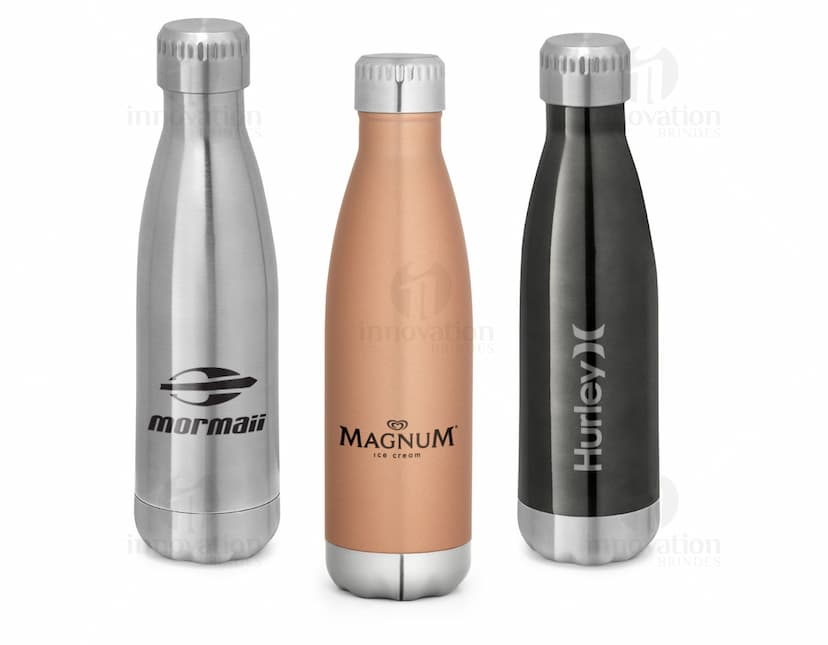 Squeeze Inox com Parede Dupla e Tampa em destaque em meio a uma coleção de garrafas, taças e outros objetos relacionados a bebidas alcoólicas. A imagem destaca a garrafa transparente de inox brilhante com tampa, contra um fundo de reflexos e objetos brilhantes.