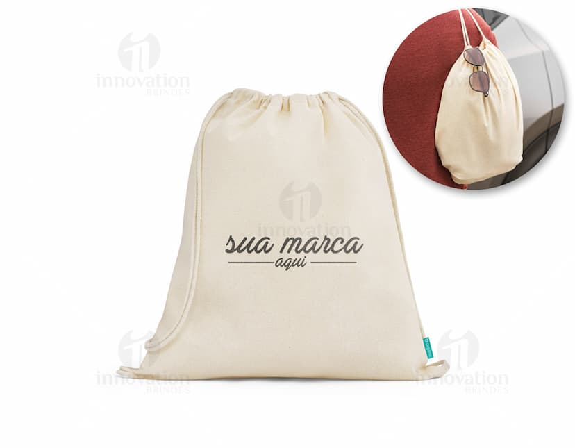 Sacola mochila de algodão orgânico 120 g, vazia e em um tom de amarelo suave. A imagem mostra a sacola aberta, com um design vintage e textura grunge. Ao redor dela, há um envelope, notas de dinheiro, uma página em branco, um livro antigo e um cartão. O cenário remete a uma atmosfera retro e nostálgica, ideal para representar um presente especial.