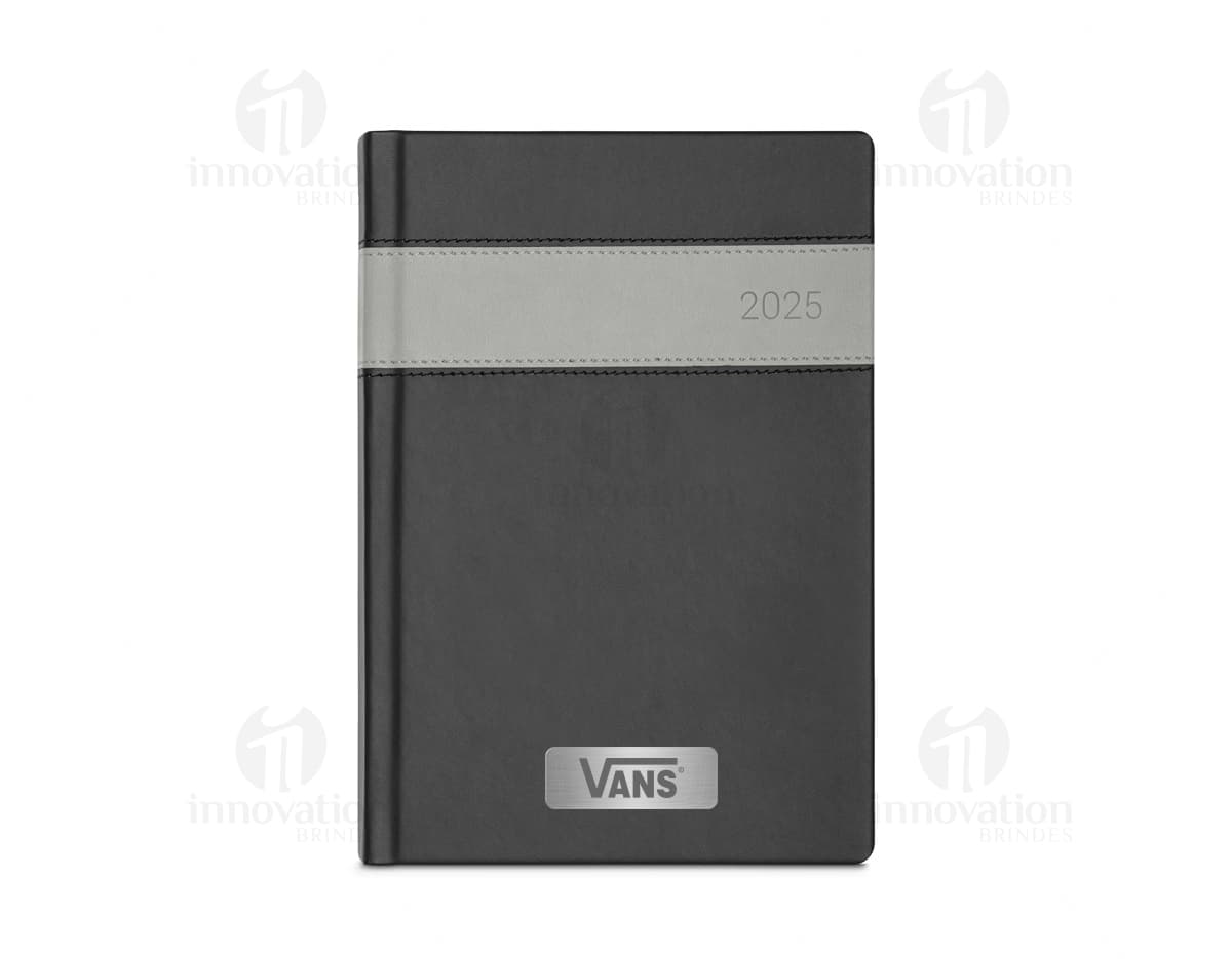 Notebook com capa de couro sintético preto, com marcador de fita colorida. O objeto está aberto, exibindo páginas em branco e tem um disco rígido externo ao lado. Há um bloco de notas, caneta e drive de armazenamento na mesa de escritório.