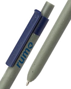 Caneta reciclada colorida feita de material metálico, com desenhos coloridos feitos a giz. Está próxima a um aparelho eletrônico e a um cigarro deitado sobre um papel, simbolizando o contraste entre a educação e os riscos à saúde do tabagismo. Ao fundo, um prédio escolar e uma coluna de metal.