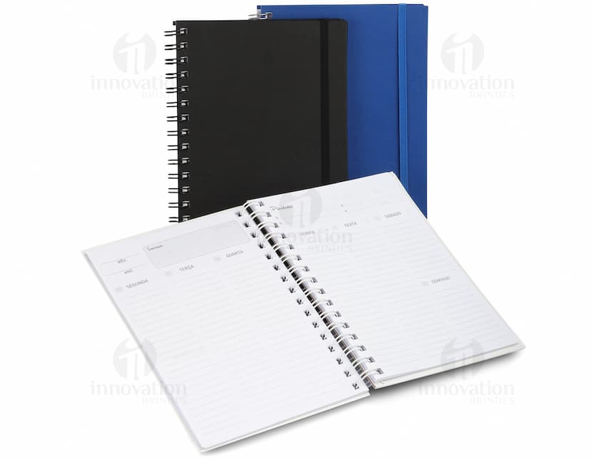 Caderno de negócios aberto com páginas em branco, papel em espiral amarelo e marrom, com espaço para escrever mensagens e lembretes. Pen e lápis ao lado do caderno, sem ninguém na imagem.
