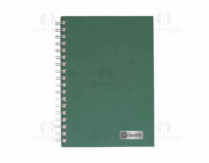 Caderno em branco aberto sobre uma mesa de escritório, com uma caneta ao lado. O caderno possui linhas para escrever e um design simples e moderno. A imagem também mostra um notebook e outros materiais de escrita ao fundo.