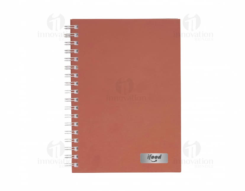 Caderno em branco aberto sobre uma mesa de escritório, com uma caneta ao lado. O caderno possui linhas para escrever e um design simples e moderno. A imagem também mostra um notebook e outros materiais de escrita ao fundo.