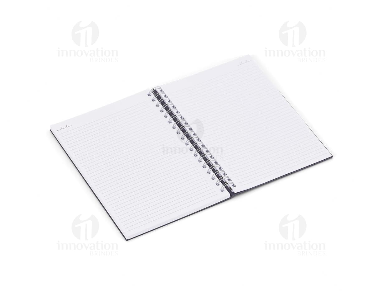 Caderno em branco aberto sobre uma mesa de escritório, com uma caneta ao lado. O caderno possui linhas para escrever e um design simples e moderno. A imagem também mostra um notebook e outros materiais de escrita ao fundo.