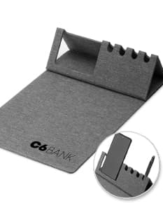 Mouse pad de couro marrom aberto em cima de uma mesa de escritório, ao redor estão um notebook preto, uma bolsa de couro, chaves, um cartão de crédito, uma carteira, um bloco de notas, um teclado preto e um mouse preto.