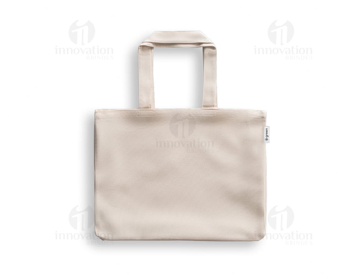 imagem de uma sacola de algodão reciclado 220g/m², com design moderno e elegante, na cor preta e prateada. O objeto está vazio, apresentando um acabamento em couro e um fecho de zíper. A embalagem é transparente e possui alças para transporte. Ideal para compras e como acessório pessoal.