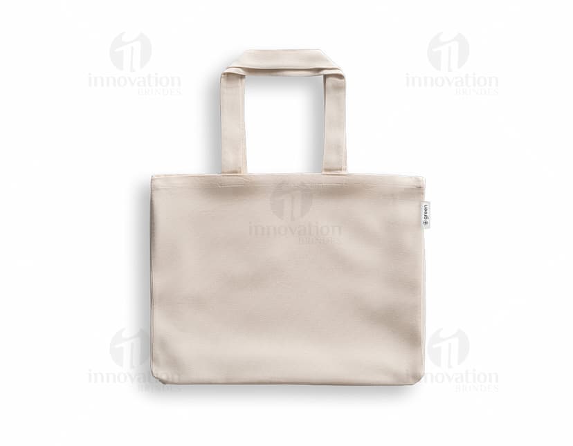 imagem de uma sacola de algodão reciclado 220g/m², com design moderno e elegante, na cor preta e prateada. O objeto está vazio, apresentando um acabamento em couro e um fecho de zíper. A embalagem é transparente e possui alças para transporte. Ideal para compras e como acessório pessoal.