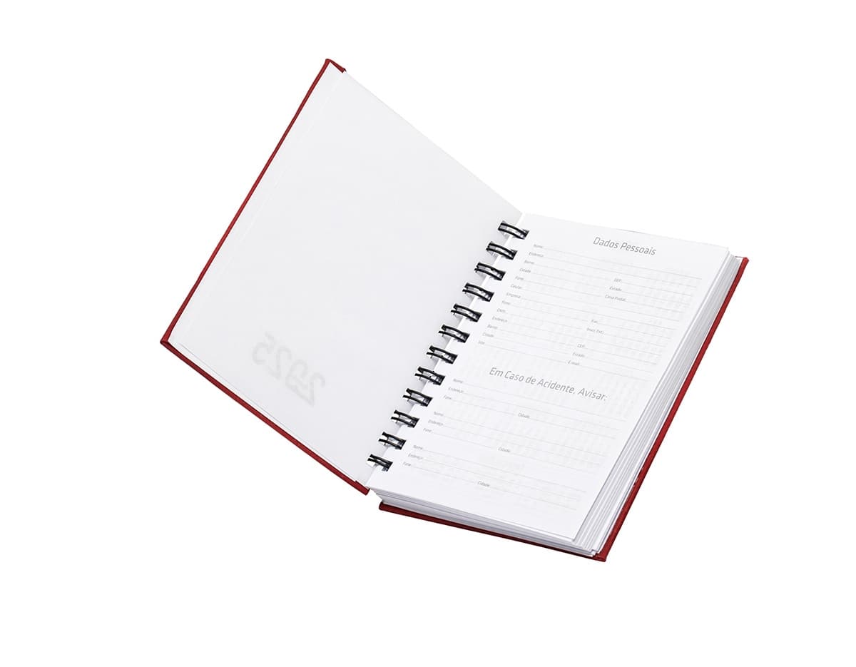 Agenda 2025 Emborrachada em uma mesa de escritório, ao lado de um notebook, dispositivo de internet, roteador, papel em branco, equipamentos de escritório e livros.