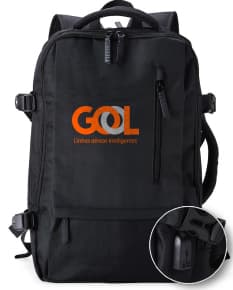 Homem de negócios usando um elegante terno preto, segurando uma mochila de nylon preta de 20 litros com USB. O acessório tem apoio nas costas, alça, e suporte para objetos.