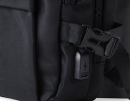 Homem de negócios usando um elegante terno preto, segurando uma mochila de nylon preta de 20 litros com USB. O acessório tem