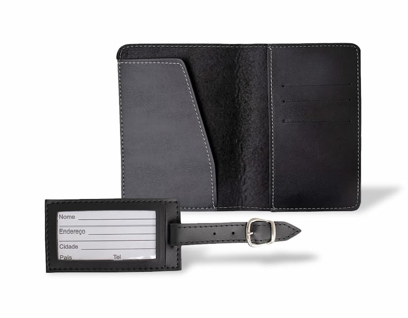 Carteira de viagem em couro marrom e porta-documentos preto abertos, contendo notas, cartões e moedas, ao lado de um notebook e um teclado eletrônico.