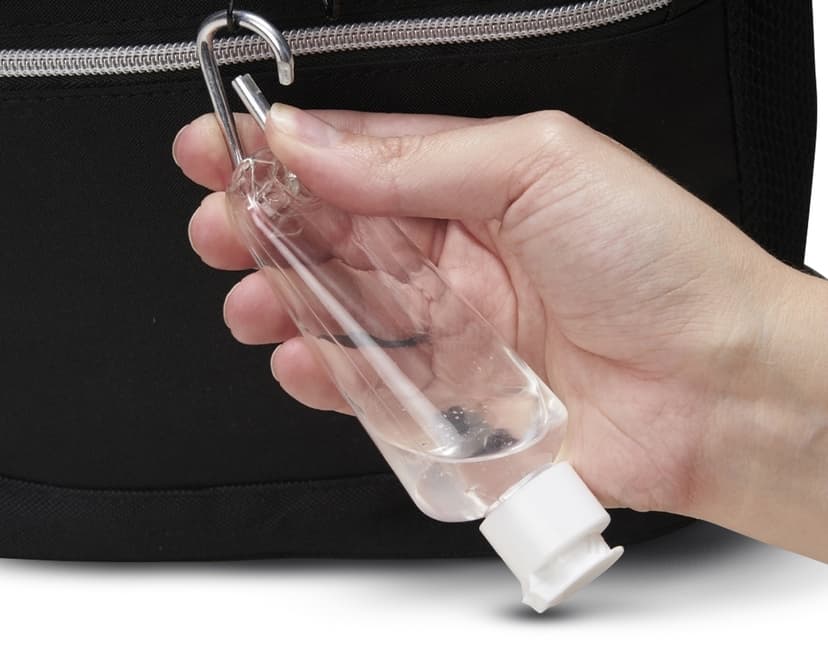 Frasco plástico 55ml com mosquetão sendo segurado por uma mão masculina, em um ambiente de escritório. A imagem mostra detalhes do frasco, como sua tampa e seu tamanho compacto, ideal para transporte.