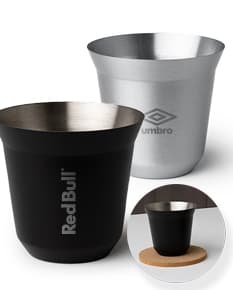 Copo de Inox de 100ml em uma mesa, ao lado de uma xícara de chá e diversos utensílios de cozinha. O copo está vazio, limpo e brilhante, com um design elegante.