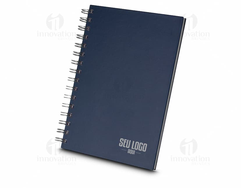Caderno de capa dura preto aberto, com folhas em branco e um lápis sobre ele. Há também um papel e um fichário ao lado. A cena se passa em um ambiente de escritório vazio.