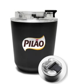 Copo térmico de 280ml em cerâmica preta e metal de cor prateada, com alça e tampa. O copo está vazio e posicionado sobre uma mesa de cozinha, ao lado de uma colher, uma jarra de café e alguns utensílios.
