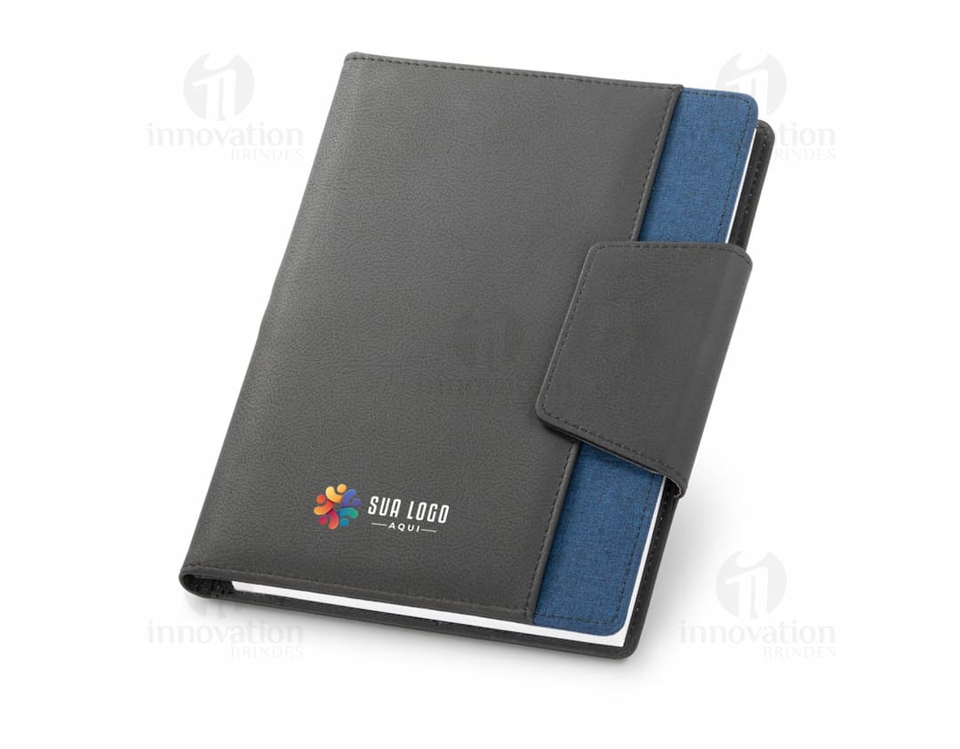 Notebook A5 com capa de couro sintético preto aberto sobre uma mesa de escritório. O caderno está vazio, com um teclado de