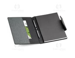 Notebook A5 com capa de couro sintético preto aberto sobre uma mesa de escritório. O caderno está vazio, com um teclado de