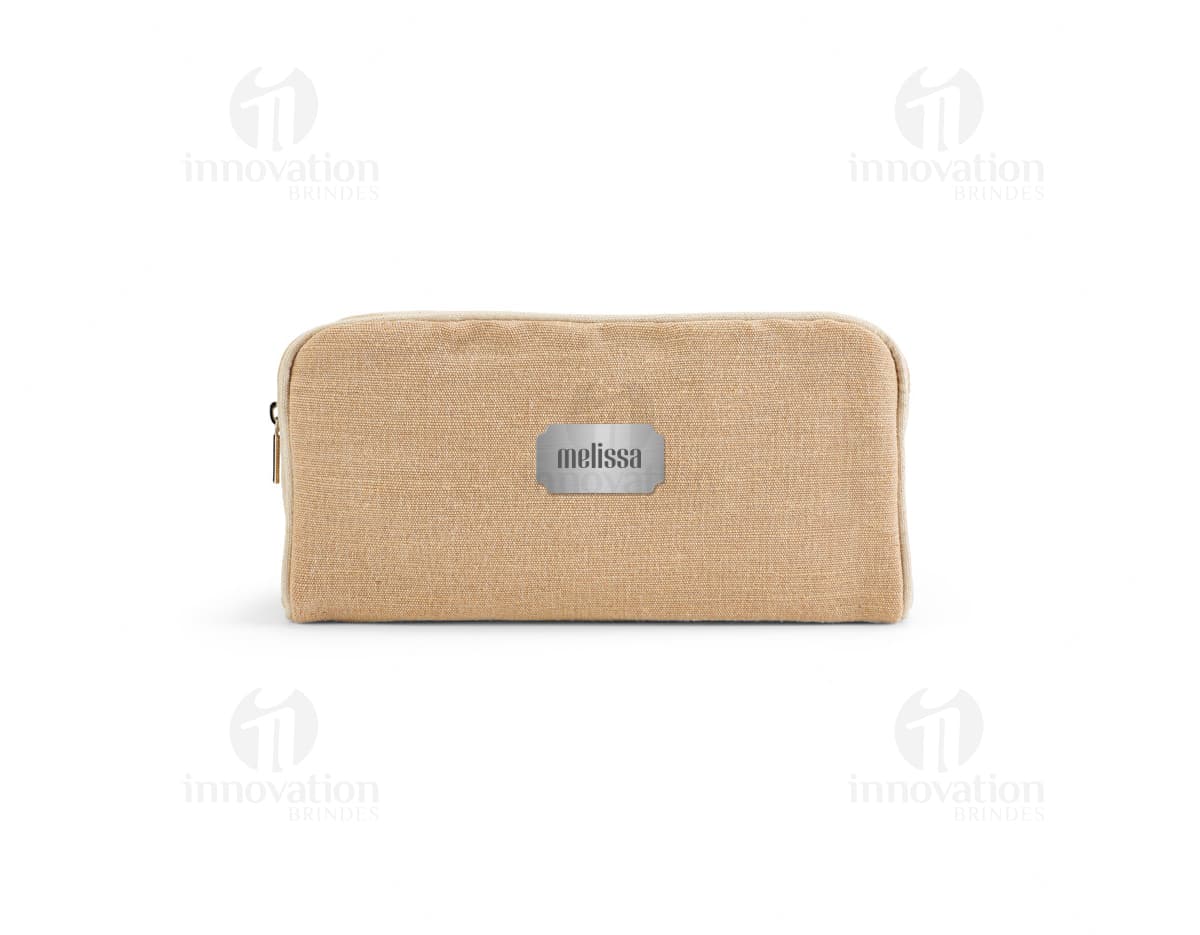 Bolsa de cosméticos marrom e preta, vazia, com fecho de zíper. Ao redor, encontram-se diversos objetos como um carimbo, um dado, uma ferramenta de modelagem, um apontador de lápis, um teclado de computador e uma chave. Há também notas de dinheiro, um cartão de crédito e um saco de compras.