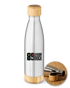 Garrafa de aço inox com tampa de cortiça, contendo líquido transparente. A garrafa está sobre uma mesa de madeira, ao lado de um copo de vinho. Ao fundo, é possível ver uvas e um rótulo de vinícola.
