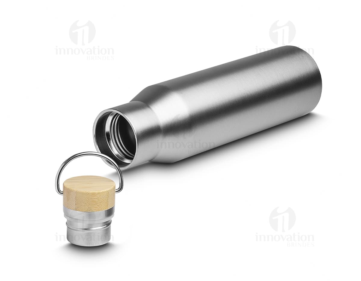 Garrafa térmica de 600ml em metal prateado, com design antigo e acabamento brilhante. O equipamento é feito de aço inoxidável e possui plug elétrico, indicando sua função de manter bebidas quentes ou frias. A embalagem possui rótulo em papel cinza com letra preta, e a tampa é de plástico preto. A garrafa térmica é mostrada em close-up, refletindo luz e sombras em sua superfície metálica.