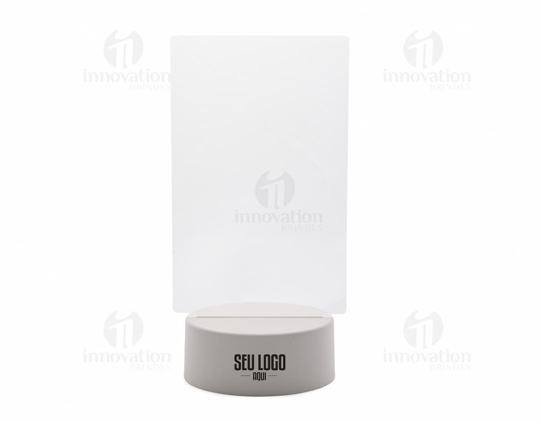 Luminária Led de Mesa em design moderno, com formato de caixa vazia e botão de acionamento. Feita em plástico transparente, possui espaço para armazenamento de mídia digital, com reflexo prateado e teclado brilhante. Ideal para utilização em escritórios e ambientes corporativos.