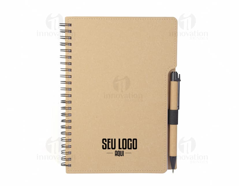 Caderno em branco com uma espiral, folhas pautadas e capa texturizada marrom. No fundo, um escritório vazio e organizado com papel, caneta e clips.