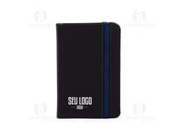 Notebook preto com external drive ao lado, sobre a mesa do escritório. A caderneta emborrachada sem pauta está aberta ao lado