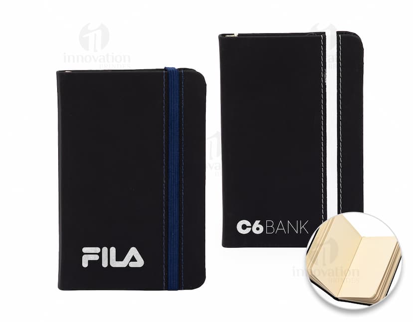 Notebook preto de couro com capa emborrachada, sem pauta, aberto em uma página em branco. Ao lado, um alto-falante preto. A imagem retrata um ambiente de escritório moderno, com foco em tecnologia e organização.
