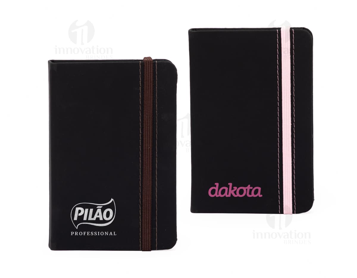 Notebook business preto em branco, com capa de couro e teclado visível. Ao lado há uma carteira de couro preto, além de livros, papéis e uma pasta de documentos. No teclado do notebook, há uma carteira aberta com dinheiro e uma nota. A imagem inclui também um estojo de escritório, um ícone de cifrão, botões de teclado e um alto-falante.