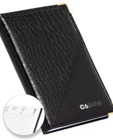 Notebook de couro preto contendo uma agenda diária para o ano de 2025, com wallet, case, paper, dinheiro em espécie e equipamentos de escritório próximos.