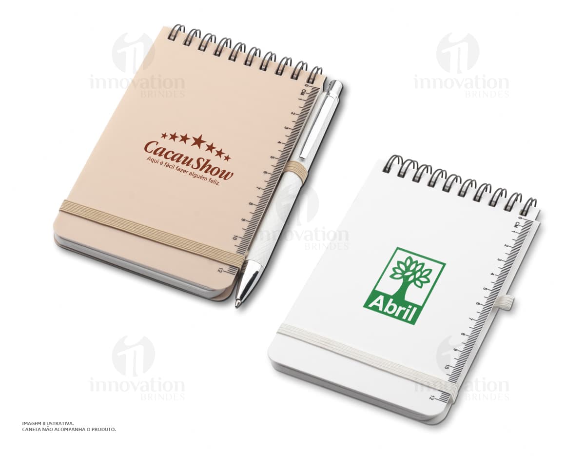 Mini caderno em 3D, com capa preta e espiral, aberto e vazio. O caderno está sobre uma mesa de escritório, ao lado de um notebook, um livro e um papel em branco. A imagem transmite a ideia de organização, estudo e trabalho.
