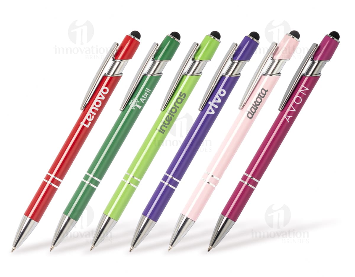 Caneta metal touch em diversas cores sobre uma mesa de escritório, ao lado de um bloco de notas, lápis e papel.