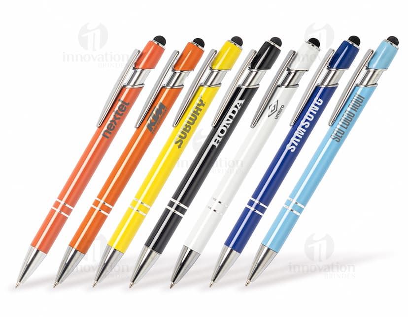 Caneta metal touch em diversas cores sobre uma mesa de escritório, ao lado de um bloco de notas, lápis e papel.