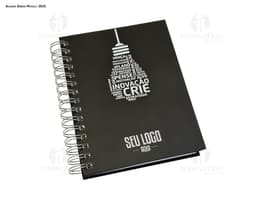 Agenda Wire-o em formato de espiral com capa preta e páginas em branco aberta em cima de uma mesa de escritório.