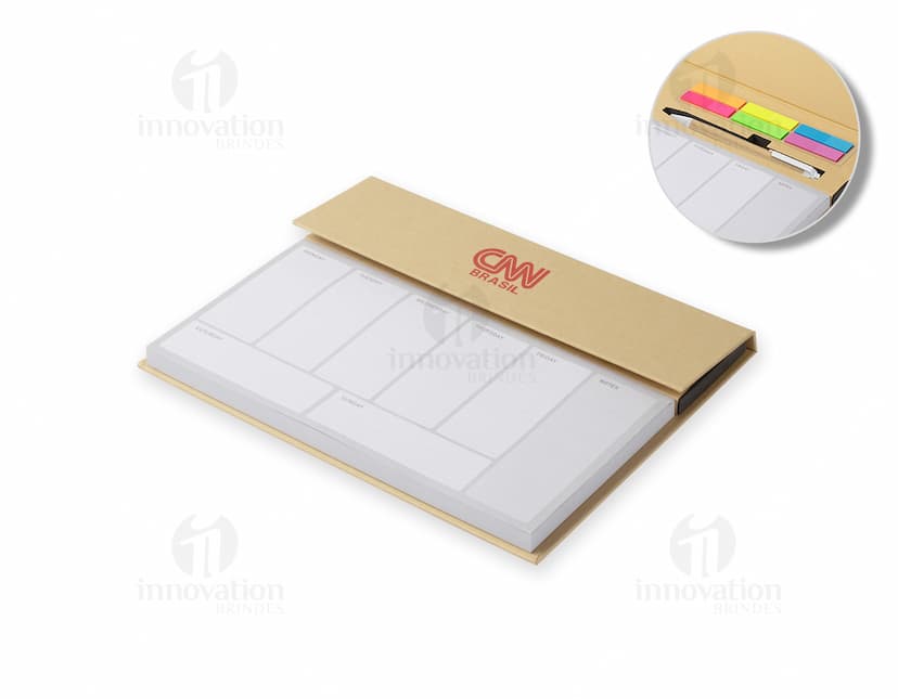 Bloco de anotações com planejamento aberto em uma mesa de escritório. No bloco, é possível ver páginas decoradas e datas planejadas. Além disso, há canetas e clips ao redor do bloco.