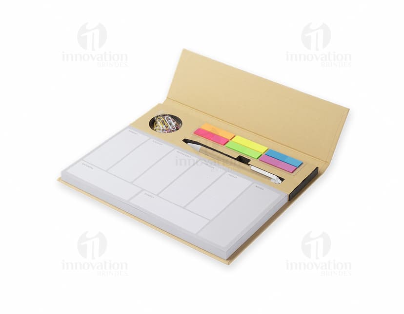 Bloco de anotações com planejamento aberto em uma mesa de escritório. No bloco, é possível ver páginas decoradas e datas planejadas. Além disso, há canetas e clips ao redor do bloco.