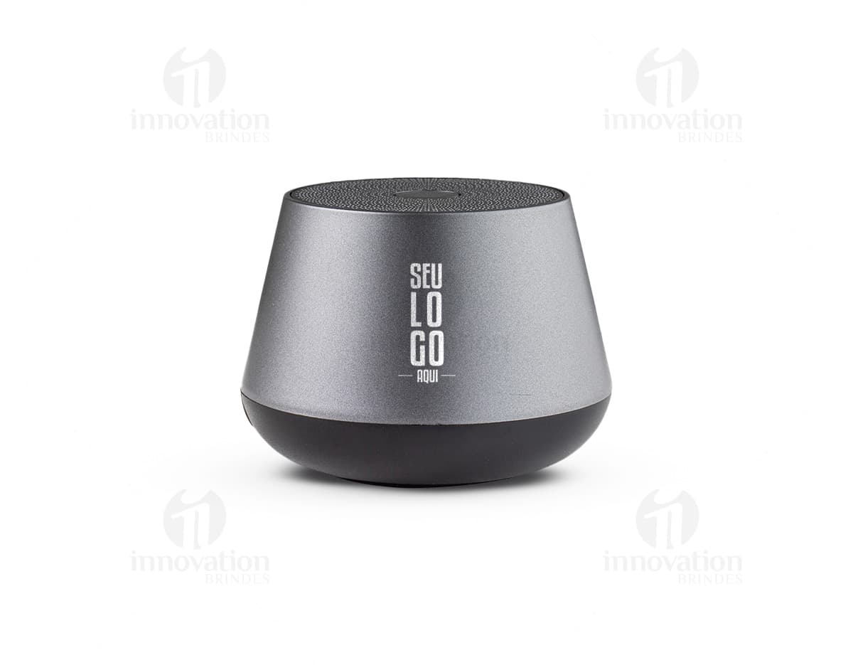Caixinha de som wireless portátil com design compacto e elegante, na cor preta. Aparelho com botões de controle e luz indicadora de funcionamento. Ideal para ouvir música em qualquer lugar.
