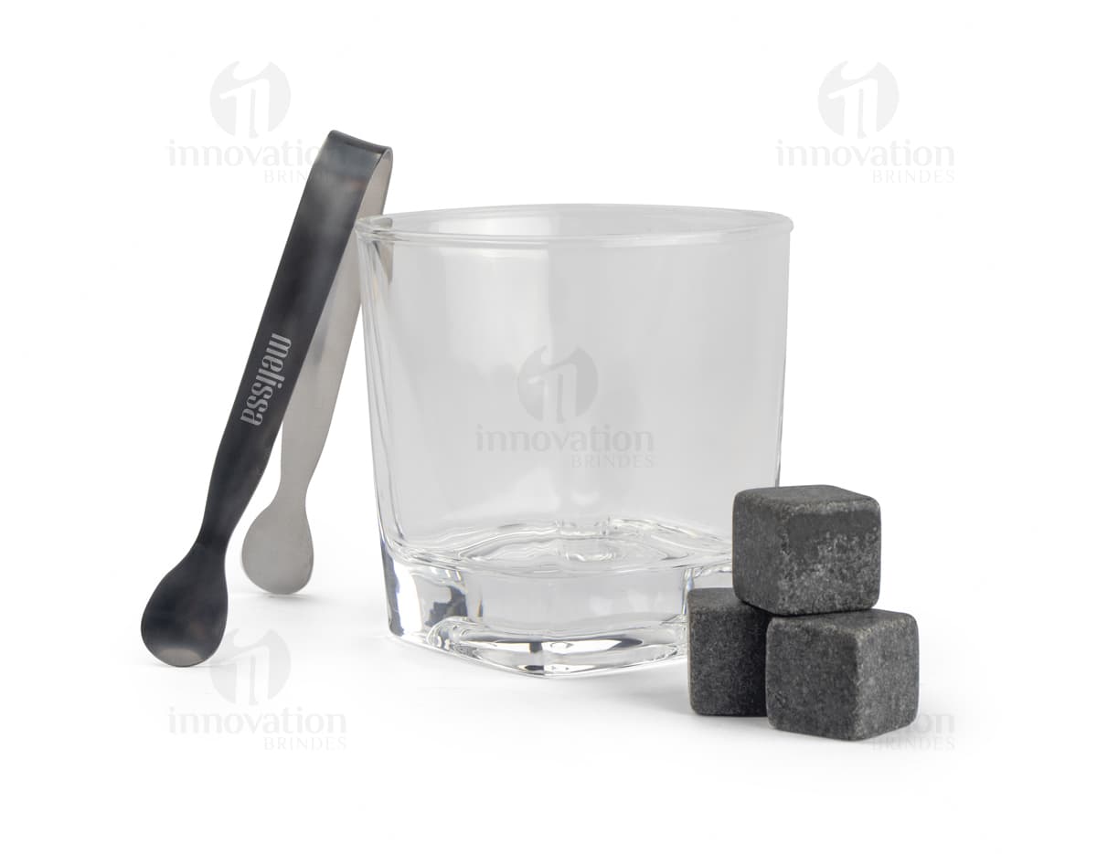 Kit Drink em uma caixa de papelão marrom. A embalagem está aberta e contém várias garrafas e copos empilhados. Ao redor da caixa, há diversos objetos de decoração e símbolos de riqueza, como um cofre, livros, um baú e uma impressora.