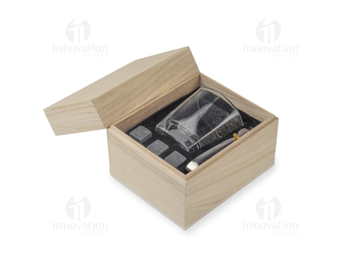 Kit Drink em uma caixa de papelão marrom. A embalagem está aberta e contém várias garrafas e copos empilhados. Ao redor da caixa, há diversos objetos de decoração e símbolos de riqueza, como um cofre, livros, um baú e uma impressora.