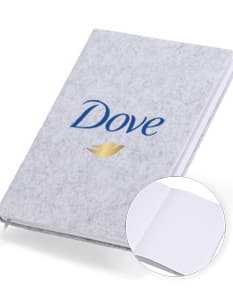 caderno A5 de feltro preto, sem pauta, aberto em uma página em branco. Ao lado, um notebook e um envelope preto. No fundo, livros e objetos de escritório.
