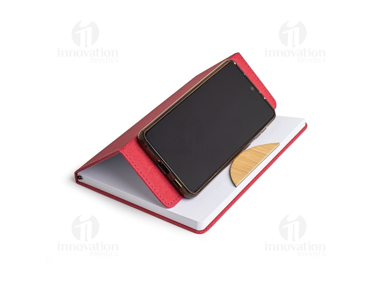 Caderneta com suporte de celular em uma mesa de escritório com notebook, papel em branco, cartão vazio, notas amarelas, livro, textos, padrões e texturas coloridas.