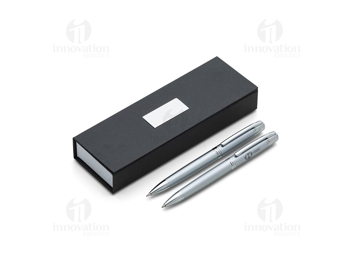 Conjunto de caneta e lapiseira de metal em fundo branco. A caneta e a lapiseira possuem detalhes cromados e são apresentadas em uma caixa elegante.