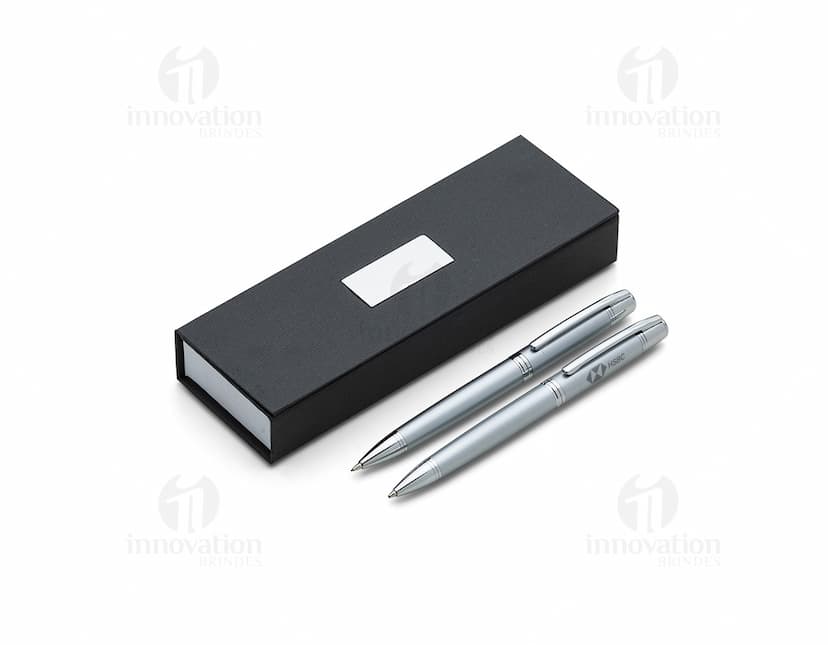Conjunto de caneta e lapiseira de metal em fundo branco. A caneta e a lapiseira possuem detalhes cromados e são apresentadas em uma caixa elegante.