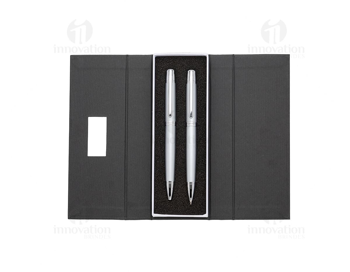 Conjunto de caneta e lapiseira de metal em fundo branco. A caneta e a lapiseira possuem detalhes cromados e são apresentadas em uma caixa elegante.