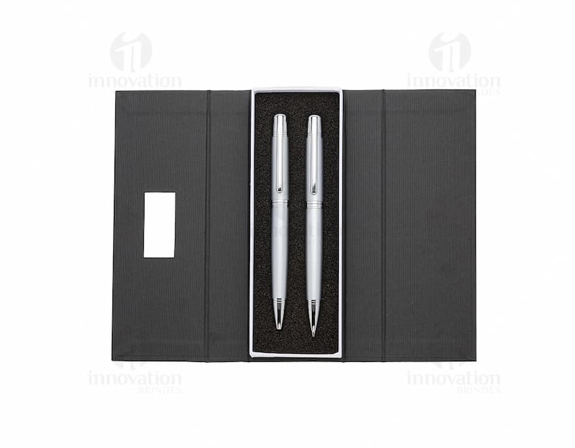 Conjunto de caneta e lapiseira de metal em fundo branco. A caneta e a lapiseira possuem detalhes cromados e são apresentadas em uma caixa elegante.