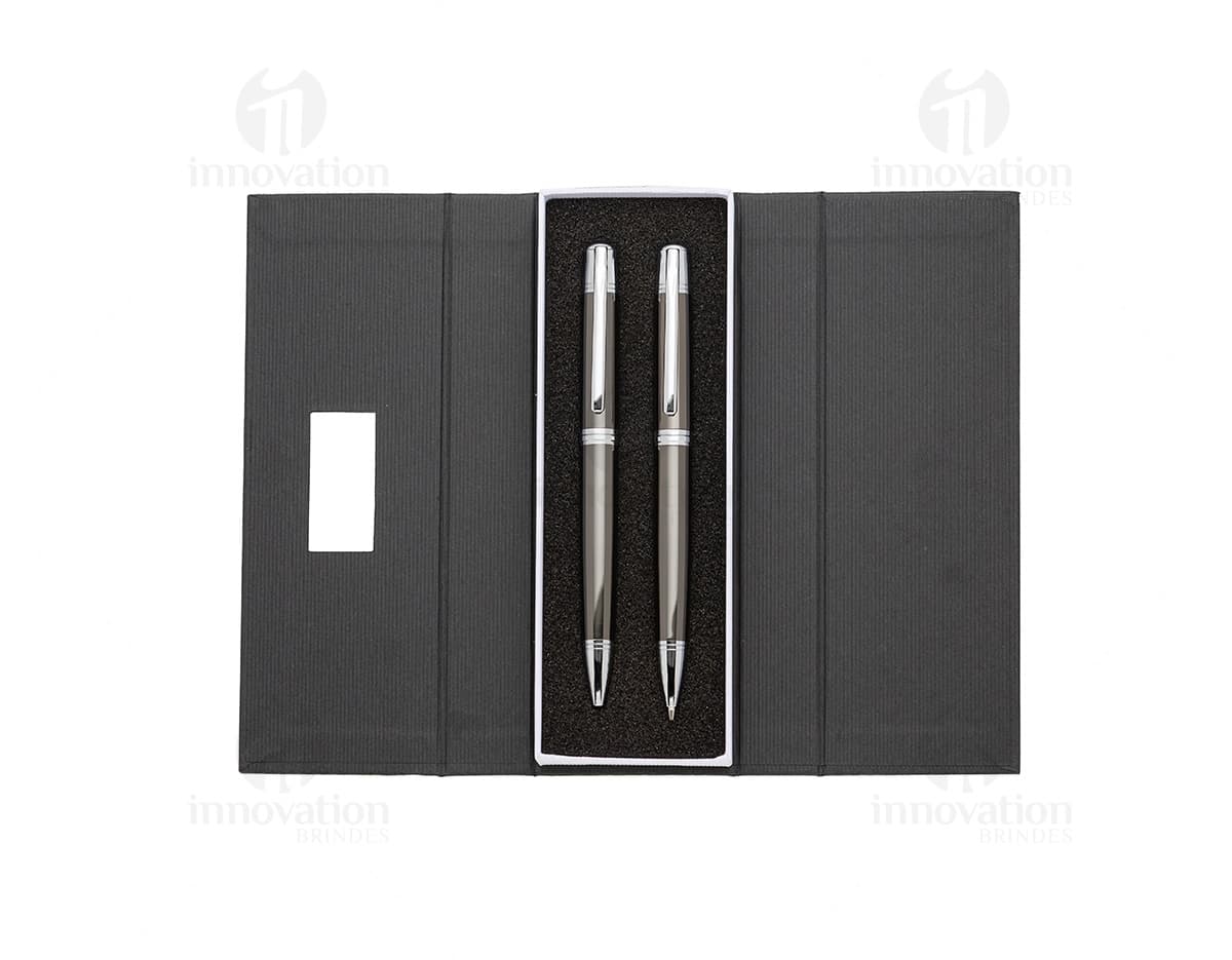 Conjunto de caneta e lapiseira de metal em fundo branco. A caneta e a lapiseira possuem detalhes cromados e são apresentadas em uma caixa elegante.