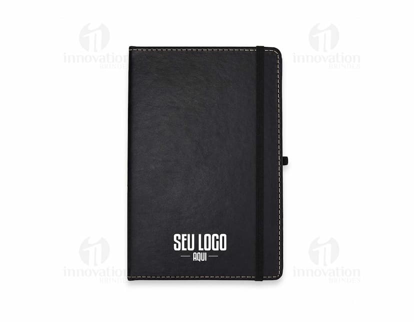 Caderneta em Couro Sintético preto com fecho magnético e papel pautado.